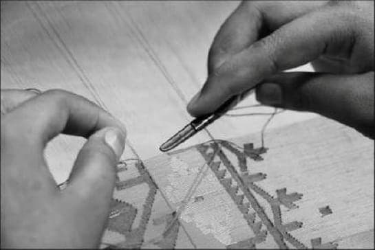 Black-and-white close-up of hands stitching Jamdani